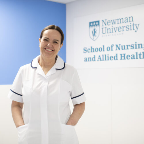 A trainee nurse at Newman standing in front of Applied Nursing signage